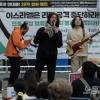 -3월 30일 오후 서울 광화문 D타워 앞에서 열린 ‘28차 팔레스타인 연대 집회’에서 팔레스타인계 미국인 아부드 애쉬, 한국인 기타리스트이자 싱어송라이터 레인보우99, 베이시스트 신지용 씨가 팔레스타인에 연대하는 공연을 하고 있다.
